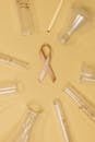 Gold ribbon for cancer awareness surrounded by lab equipment on a yellow background.